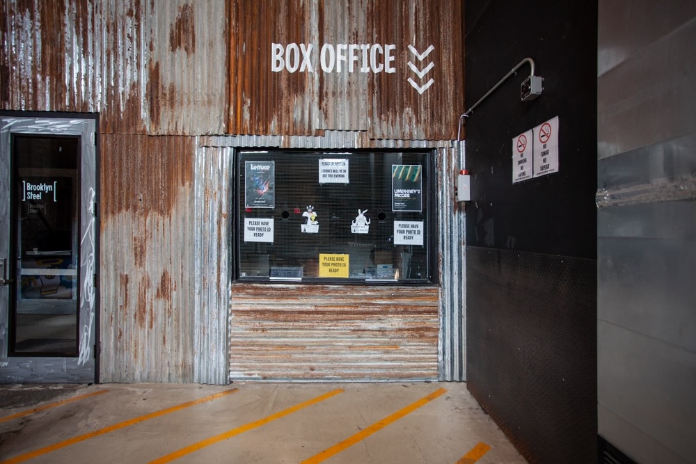 Ticket booth of Brooklyn Steel showcasing rustic corrugated panels, new tiles, modern doors, concrete slab, and glass elements