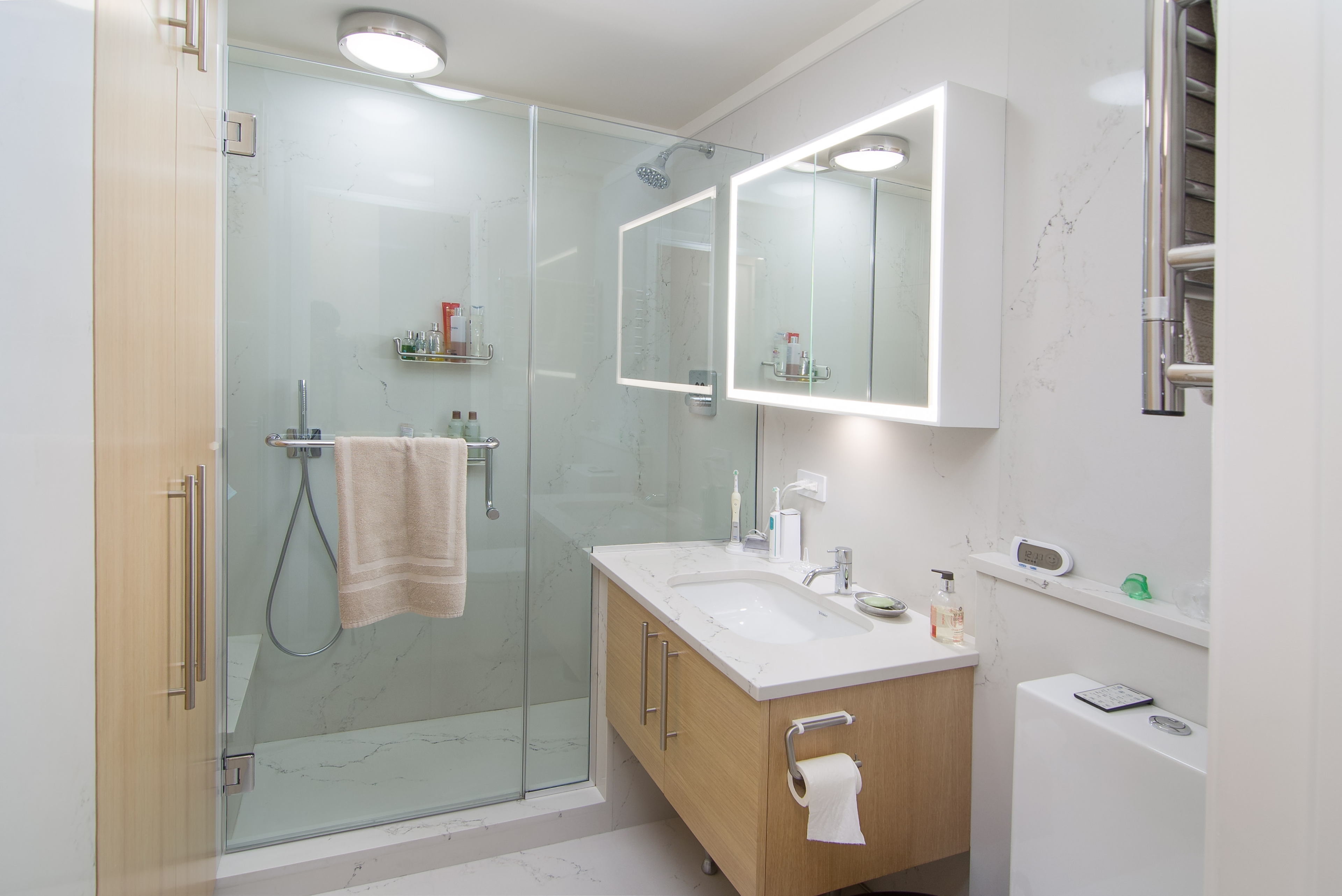 Renovated modern bathroom showcasing new stones, modern light fixtures, a walk-in shower, new bathroom cabinets, and a European heating radiator.