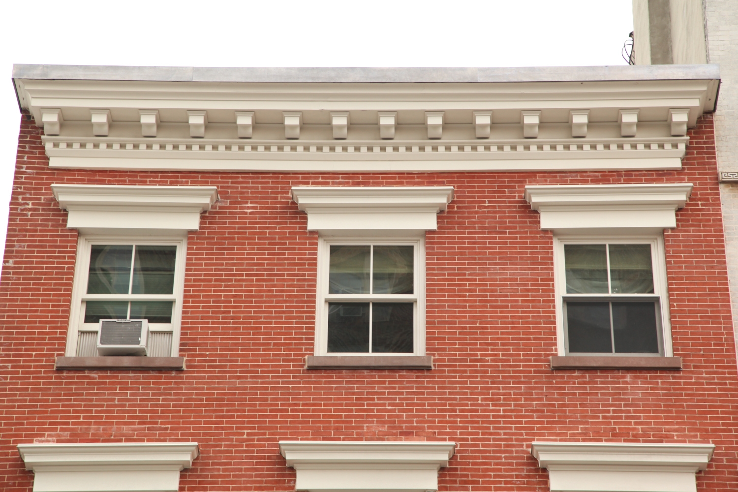 Exterior view of a New York City building displaying Jepol Construction's expert restoration work on a cornice, brickwork, ornamental window lintel, and window sills.