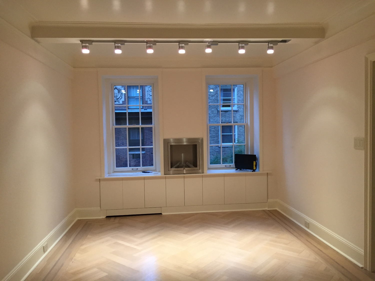 Interior view of an apartment in Manhattan featuring new partitions, wall bench cabinets, refinished flooring, freshly painted walls, new lighting, and an electric fireplace
