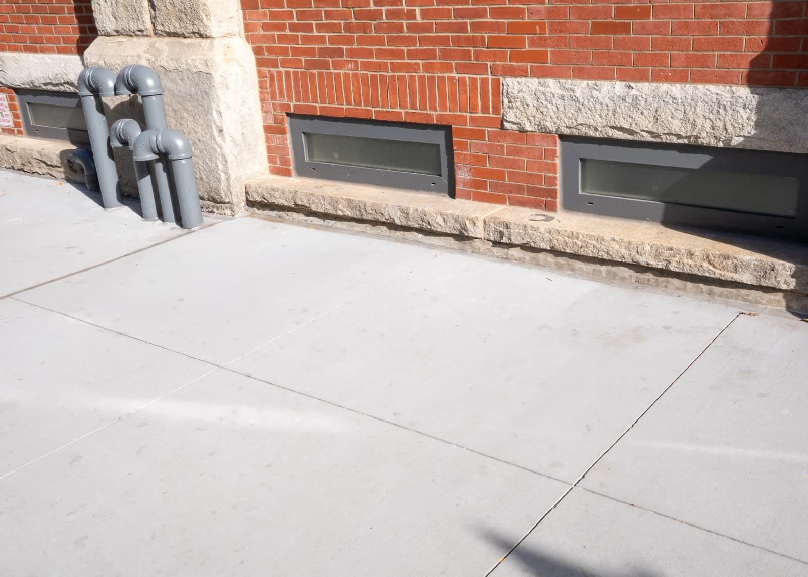 Concrete sidewalk fitted around basement windows and the building edge